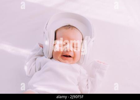 Das Kind trägt Kopfhörer. Frohes Baby. Ein neugeborenes Baby. Weiß auf Weiß Stockfoto