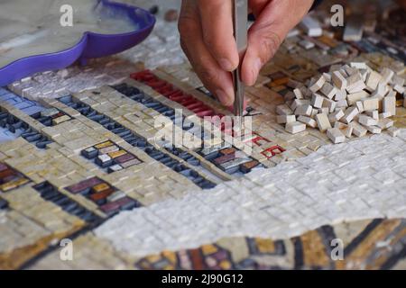 Die Hand eines jordanischen Mosaikherstellers in Aktion, während sie die winzigen Kacheln mit einer Pinzette zu einem Wandbild klebt Stockfoto