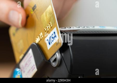 Batumi, Georgien - 5 2022. April: Nahaufnahme eines Zahlungsterminals mit der Hand einer Person, die eine Visumkarte aus Kunststoff hält Stockfoto