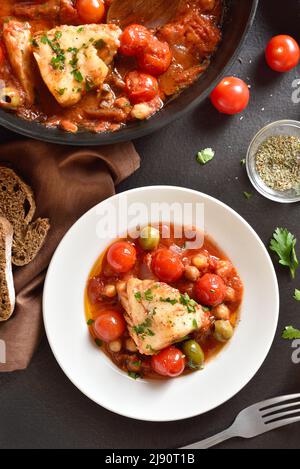 Kabeljaueintopf mit Kichererbsen, Kirschtomaten und Oliven auf dem Teller auf dunklem Steingrund. Draufsicht, flach liegend Stockfoto