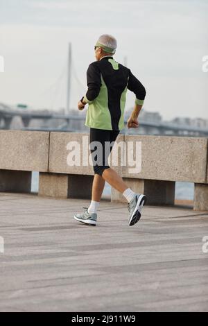 Nicht erkennbare cporty älterer Mann entlang am Meer im Morgen, vertikaler Ausführung Stockfoto