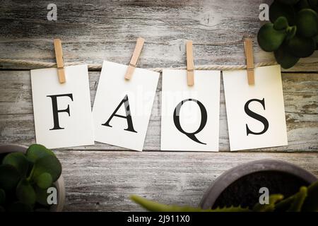 Eine Reihe von gedruckten Karten mit dem Wort FAQs auf einem alten Holzhintergrund. Stockfoto