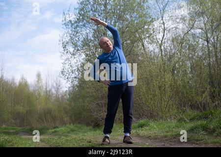 Seniorläufer mit Armreif beim Stretching. Frühling Natur. Gesunde Lebensweise im Alter. Stockfoto