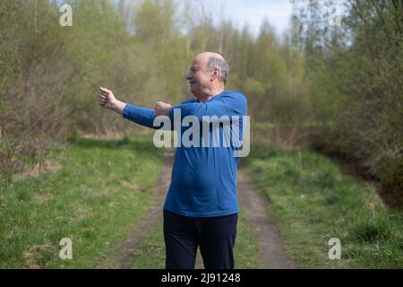 Seniorläufer mit Armreif beim Stretching. Frühling Natur. Gesunde Lebensweise im Alter. Stockfoto