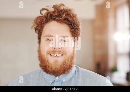 Porträt eines lächelnden Rothaarigen mit Bart und Schnurrbart, der im modernen Büro steht Stockfoto