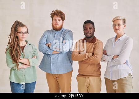Eine Gruppe von vier ernsthaften jungen multiethnischen Arbeitern, die mit gekreuzten Armen stehen und die Kamera betrachten Stockfoto