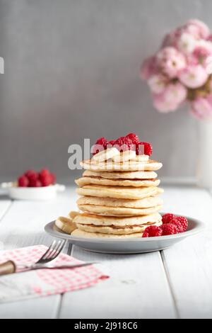 Amerikanische Pfannkuchen mit Himbeeren und Bananen auf hellem, minimalem Hintergrund. Leckere Pfannkuchen auf Holztisch mit Früchten. Stockfoto