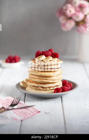 Amerikanische Pfannkuchen mit Himbeeren und Bananen auf hellem, minimalem Hintergrund. Leckere Pfannkuchen auf Holztisch mit Früchten. Stockfoto