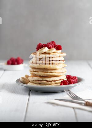 Amerikanische Pfannkuchen mit Himbeeren und Bananen auf hellem, minimalem Hintergrund. Leckere Pfannkuchen auf Holztisch mit Früchten. Stockfoto