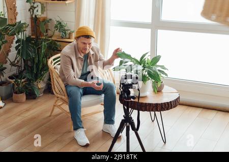 Blogger mittleren Alters mit Videoaufnahme in gemütlicher Inneneinrichtung im Boho-Stil. Mann, der zu Hause Videos aufzeichnet Stockfoto
