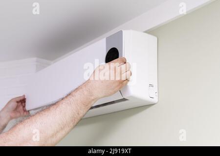 Ein Mann entfernt die Abdeckung der Klimaanlage für Reparaturen in Innenräumen Stockfoto