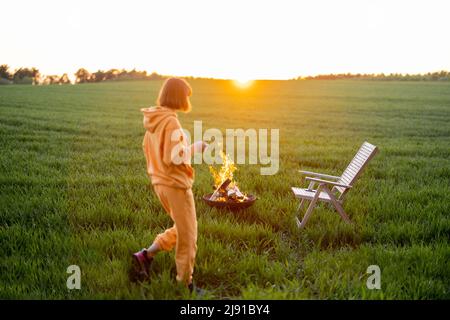 Frau, die sich am Kamin auf dem grünen Feld bei Sonnenuntergang entspannt Stockfoto