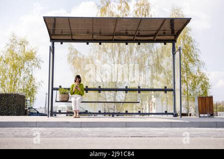 Frau mit Blumentopf an der modernen Bushaltestelle Stockfoto