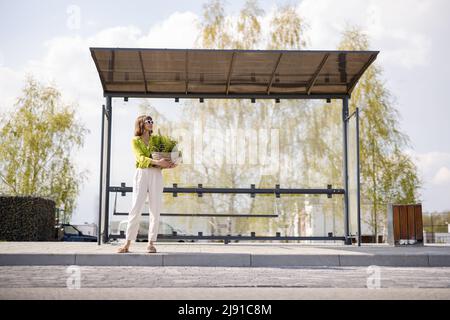 Frau mit Blumentopf an der modernen Bushaltestelle Stockfoto