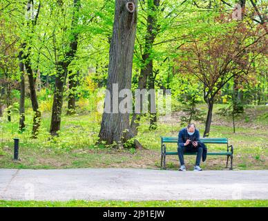 Bukarest, Rumänien - 04.15.2022: Einzelner isolierter Mann sitzt auf einer Bank im Park von König Mihai I (Herestrau) Stockfoto