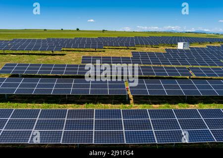 Luftbild Photovoltaik-Paneele Park auf grünen Feld in Nordgriechenland. Blauer Himmel, der sich in Reihen von Sonnenkollektoren widerspiegelt. Futuristisches alternatives Kraftwerk. S Stockfoto