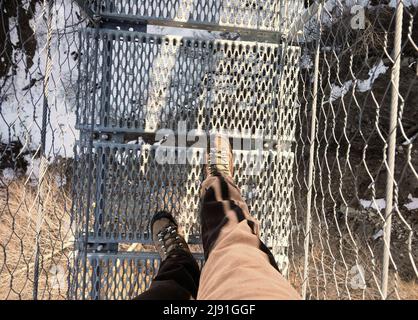 Leichte Stiefel und menschliche Beine auf der spektakulären Hängebrücke aus Stahlseilen und Metallsesseln Stockfoto