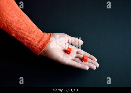 Rote Würfel in der männlichen Hand zeigen nach unten. Speicherplatz kopieren. Nahaufnahme. Selektiver Fokus. Stockfoto