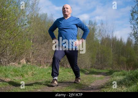 Seniorläufer mit Armreif beim Stretching. Frühling Natur. Gesunde Lebensweise im Alter. Stockfoto