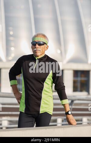 Vertikale mittellang Portraitfotos der aktiven starken älterer Mann mit schwarzen und grünen Trainingsanzug in Pause während des Trainings Stockfoto