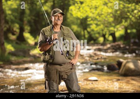 Reifer Fischer, der mit einer Angelrute neben einem Fluss posiert Stockfoto
