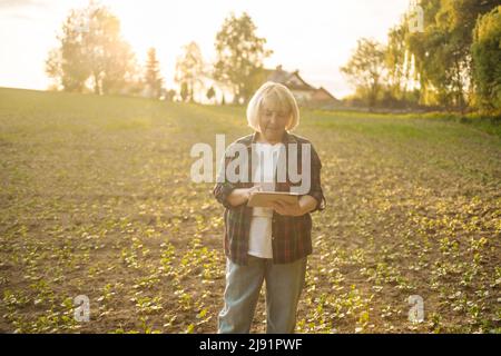 Porträt der Agronomin fermer Frau, die Sojabohnenpflanzen auf dem Feld untersucht. Erfolgreiche Bio-Lebensmittelproduktion und -Anbau. Stockfoto