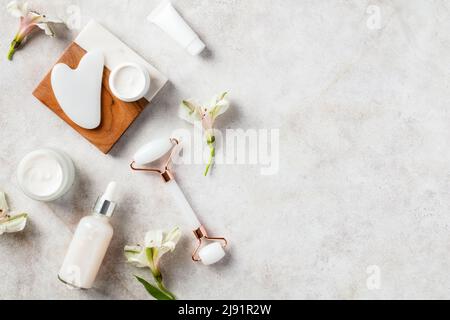 Gesichtsbehandlung Naturkosmetik auf Steintisch. Flat Lay Jade Face Roller, Gua Sha, Serum, Feuchtigkeitscreme. Stockfoto