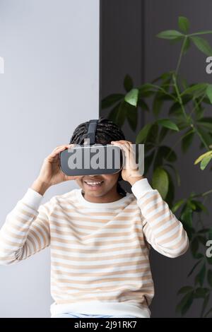 Junge erstaunt aufgeregt afro Mädchen trägt VR-Helm entspannen mit Virtual Reality auf Fensterbank zu Hause Stockfoto