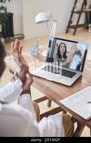 Vertikale, hochwinkelige Aufnahme eines modernen afroamerikanischen Arztes, der vor dem Laptop am Schreibtisch sitzt und einen Online-Videoanruf zeigt Stockfoto