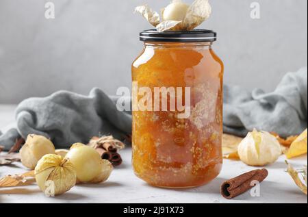 Hausgemachte transparente Physalis-Marmelade mit Zimt in einem Glas auf hellgrauem Hintergrund Stockfoto