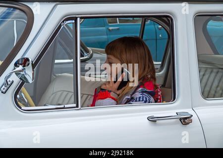 Dnipro, Ukraine - 06. Oktober 2013: Minderjähriges Mädchen Stahl Autoschlüssel von ihrem Vater und stieg hinter das Steuer. Sie rühmt sich mit ihren Freunden auf dem Handy, dass Stockfoto