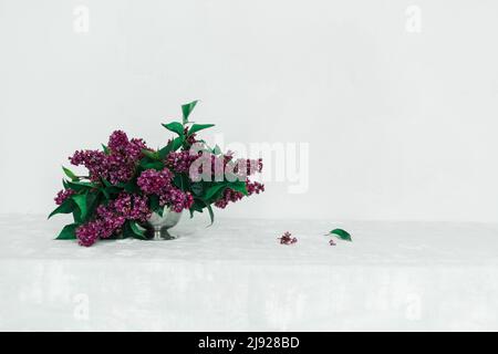 Lila Blumenarrangement auf einem Tisch mit einer grauen Tischdecke an einer weißen Wand Stockfoto