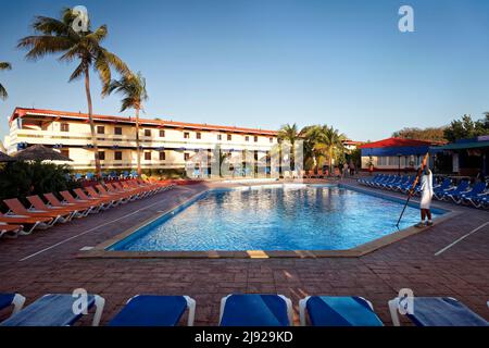 Mann reinigt Swimmingpool, Sonnenliege, hinter dem Hotelgebäude, Sonnenschirm, Kokospalme (Cocos nucifera), Hotel Club Amigo Costasur, Trinidad, Trinidad Stockfoto