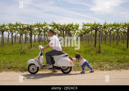 Schönes Bild von einem kleinen Mädchen, das mit ihrem Vater ein Motorrad schiebt, dem das Benzin ausgegangen war. Verweis auf teuren Kraftstoff. Stockfoto