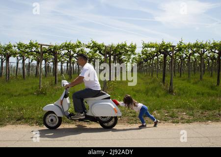 Schönes Bild von einem kleinen Mädchen, das mit ihrem Vater ein Motorrad schiebt, dem das Benzin ausgegangen war. Verweis auf teuren Kraftstoff. Stockfoto