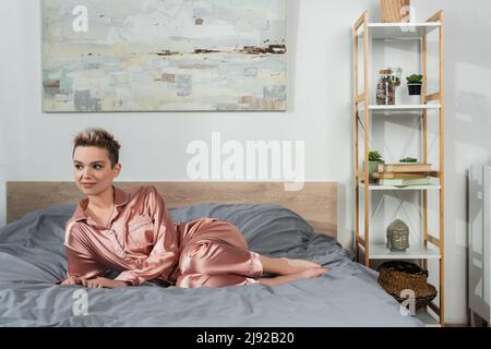 In voller Länge der Panger Person in Satin Schlafanzug Blick weg auf das Bett zu Hause Stockfoto