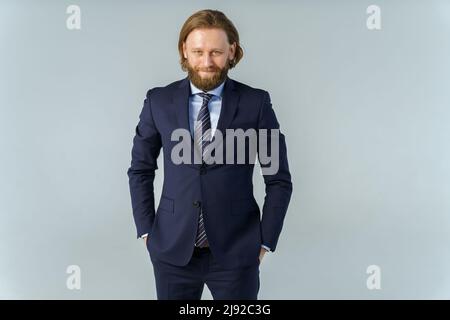 Ein hübscher, brutaler bärtiger und langhaariger Mann, ein stilvoller Geschäftsmann auf weißem Hintergrund Stockfoto