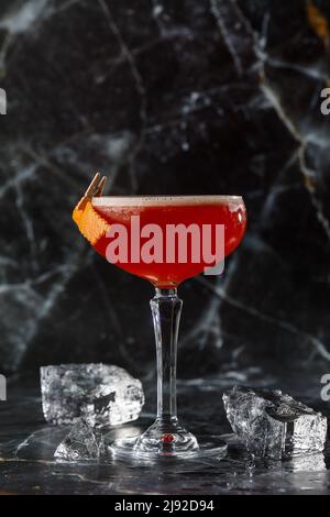 Ein rot-saurer Cocktail in einem Coupé-Glas, garniert mit einer Orangenschale. Clover Club mit importiertem Gin. Auf schwarzem Marmorboden. Stockfoto