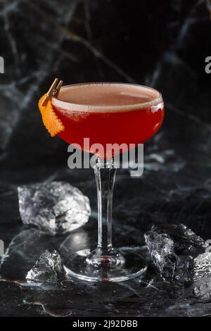 Ein rot-saurer Cocktail in einem Coupé-Glas, garniert mit einer Orangenschale. Clover Club mit importiertem Gin. Auf schwarzem Marmorboden. Stockfoto