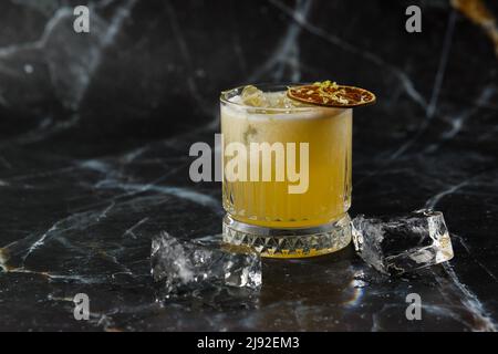 Fruchtmixologie mit Mezcal und trockenem Kalk auf schwarzem Marmorboden. Cocktails in warmen Farben. Mezcal-Cocktail Stockfoto