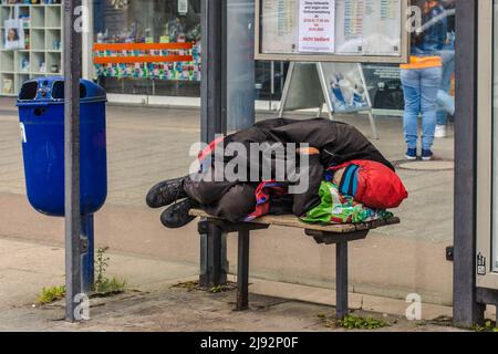 WETZLAR, DEUTSCHLAND - 23. APRIL 2022: Obdachloser liegt auf einem Sitz einer öffentlichen Bushaltestelle Stockfoto