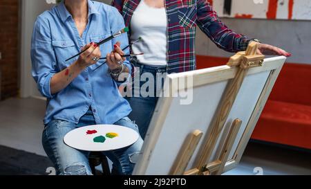 Zwei Freundinnen oder eine Frau mit ihrem Mentor Art Professor kaukasische reife Schwestern lehren und lernen, wie man beim Malen hilft Stockfoto