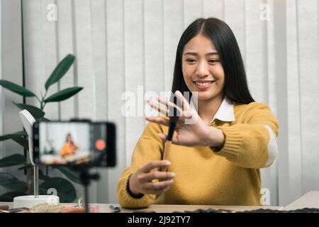 Junge asiatische Frau vloggt sich über Beauty-Produkte mit einem Video für ihren Blog über Kosmetik mit Handy-Kamera zu Hause machen. Stockfoto