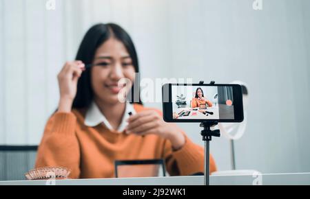 Junge asiatische Frau vloggt sich über Beauty-Produkte mit einem Video für ihren Blog über Kosmetik mit Handy-Kamera zu Hause machen. Stockfoto