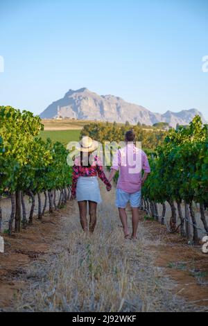Weinbergslandschaft bei Sonnenuntergang mit Bergen in Stellenbosch, nahe Kapstadt, Südafrika. Weintrauben auf der Weinrebe in einem Weinberg, Paar Mann und Frau beim Spaziergang in Vineyard in Stellenbosch, Südafrika Stockfoto