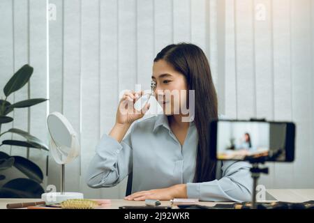 Junge asiatische Frau vloggt sich über Beauty-Produkte mit einem Video für ihren Blog über Kosmetik mit Handy-Kamera zu Hause machen. Stockfoto