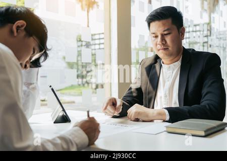 Der männliche Vorgesetzte spricht oder erklärt, dass er den Mitarbeiter entlassen muss, während ihm ein Rücktrittsschreiben ausgehändigt wird. Stockfoto