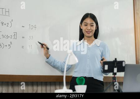 Der Lehrer erklärt die Zahlen auf dem Brett, während er mit Studenten online telefoniert. Stockfoto