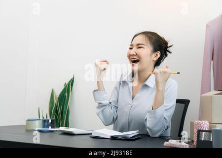 Junge asiatische Unternehmer handeln vor Freude, als sie ihre Kleidung gezielt verkaufen. Stockfoto