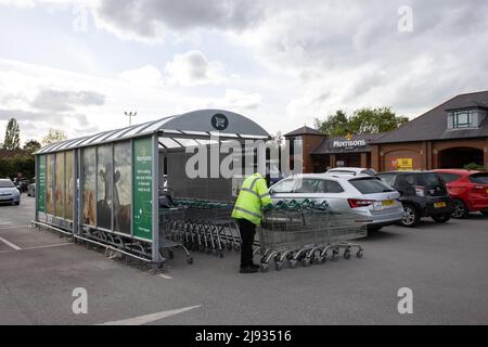 Mann in gelber reflektierender Weste bewegt Einkaufswagen am Morrisons Supermarkt Starbeck Store Parkplatz Stockfoto